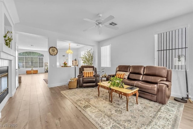 living area with a ceiling fan, visible vents, baseboards, a glass covered fireplace, and light wood-style floors