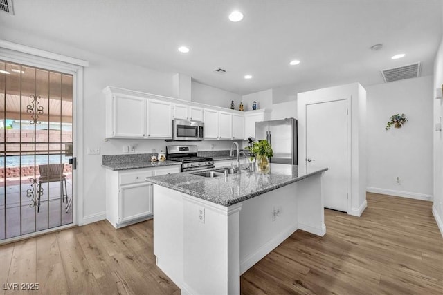kitchen featuring a sink, light wood finished floors, stainless steel appliances, baseboards, and visible vents