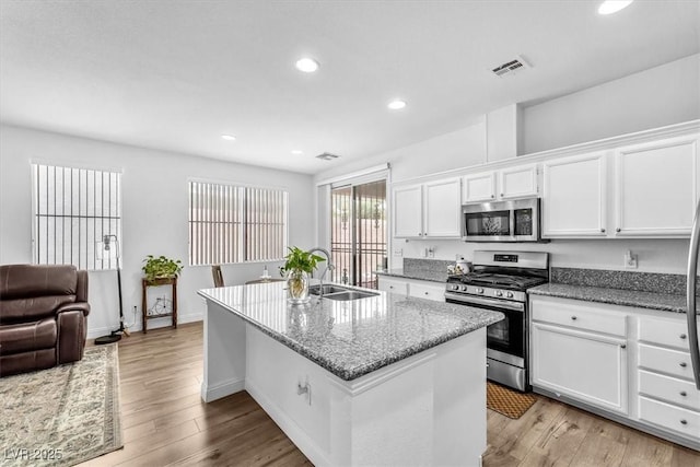 kitchen with a sink, an island with sink, stainless steel appliances, white cabinetry, and visible vents