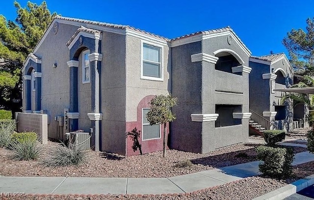 view of side of property with central air condition unit, stucco siding, and a tiled roof