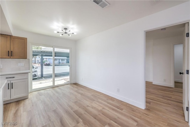unfurnished dining area featuring baseboards, light wood-style flooring, a chandelier, and visible vents