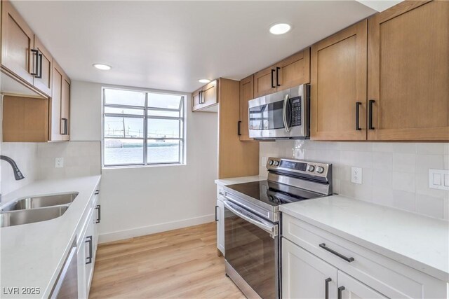 kitchen featuring baseboards, light countertops, a sink, light wood finished floors, and appliances with stainless steel finishes
