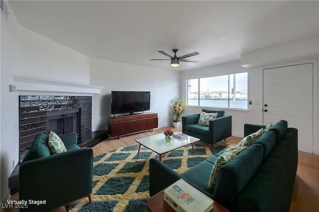 living room featuring a brick fireplace, wood finished floors, and ceiling fan