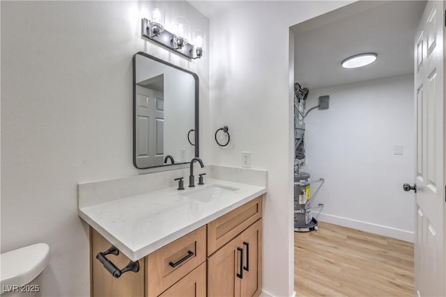 half bath with vanity, baseboards, wood finished floors, and toilet