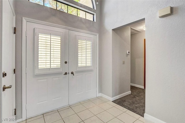 entryway with baseboards, a high ceiling, light tile patterned flooring, and light colored carpet