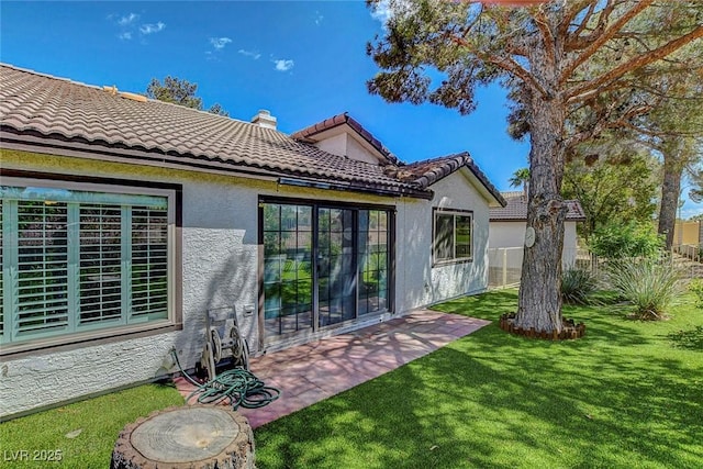 rear view of property with a yard, a tiled roof, a patio area, and stucco siding