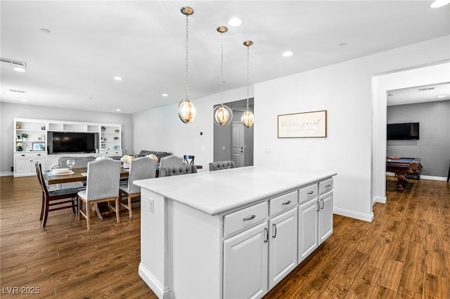 kitchen with dark wood-style floors, light countertops, a kitchen island, hanging light fixtures, and open floor plan