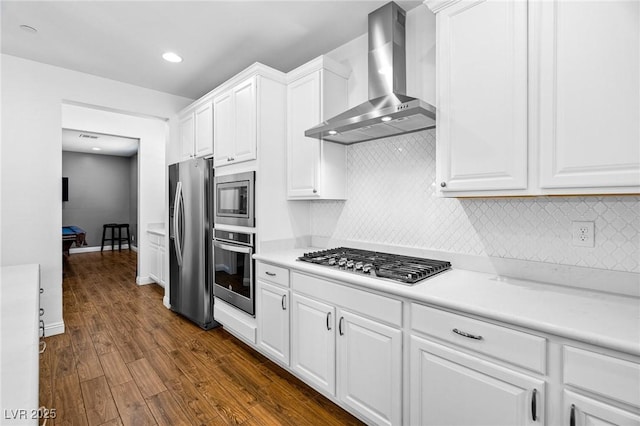 kitchen with stainless steel appliances, wall chimney exhaust hood, dark wood-style flooring, white cabinets, and light countertops