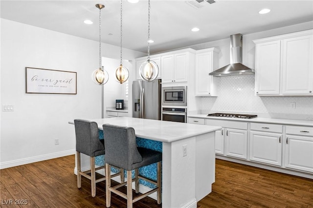 kitchen with appliances with stainless steel finishes, wall chimney range hood, a center island, dark wood-style flooring, and light countertops