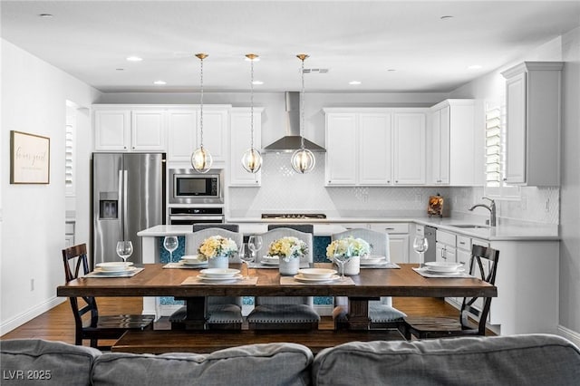 kitchen with appliances with stainless steel finishes, wall chimney range hood, a sink, light countertops, and decorative backsplash