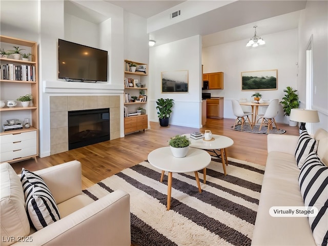 living area featuring visible vents, built in shelves, a tiled fireplace, light wood finished floors, and a notable chandelier
