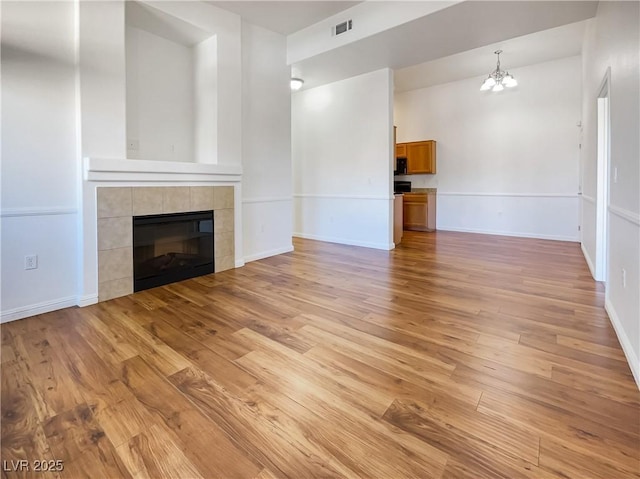 unfurnished living room featuring visible vents, an inviting chandelier, baseboards, light wood-type flooring, and a tile fireplace