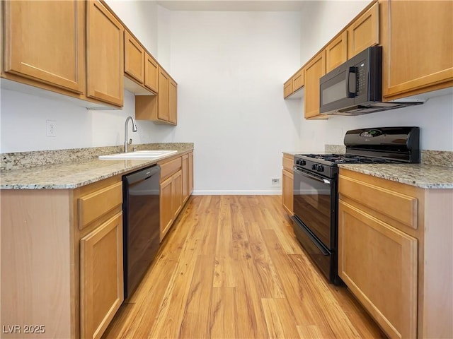 kitchen featuring light wood-style floors, baseboards, light stone counters, a sink, and black appliances