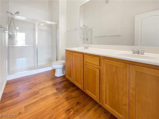 bathroom featuring double vanity, a sink, wood finished floors, and a shower stall