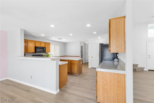 kitchen with light wood-style flooring, freestanding refrigerator, a peninsula, baseboards, and recessed lighting