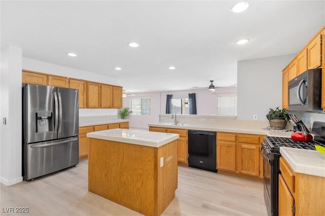 kitchen with a peninsula, a kitchen island, light wood-type flooring, recessed lighting, and black appliances
