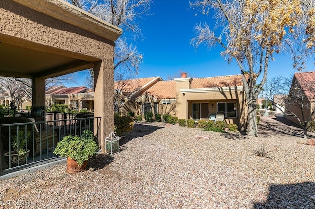 rear view of house with a chimney, stucco siding, a tile roof, and fence