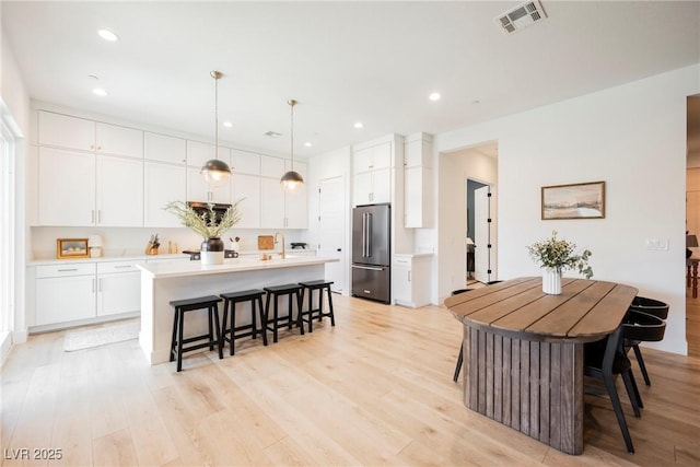 kitchen featuring a kitchen breakfast bar, a kitchen island, visible vents, high quality fridge, and light countertops