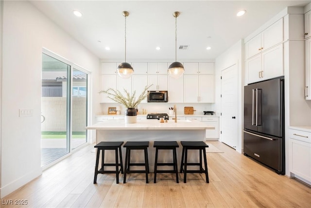 kitchen with visible vents, high end fridge, a kitchen breakfast bar, stainless steel microwave, and light wood finished floors