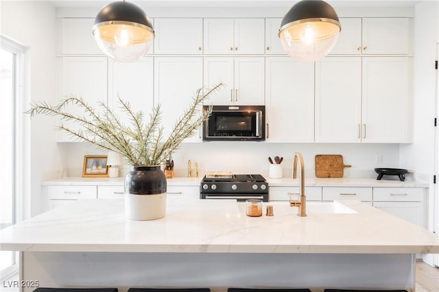 kitchen with a breakfast bar area, white cabinetry, built in microwave, and black gas stove