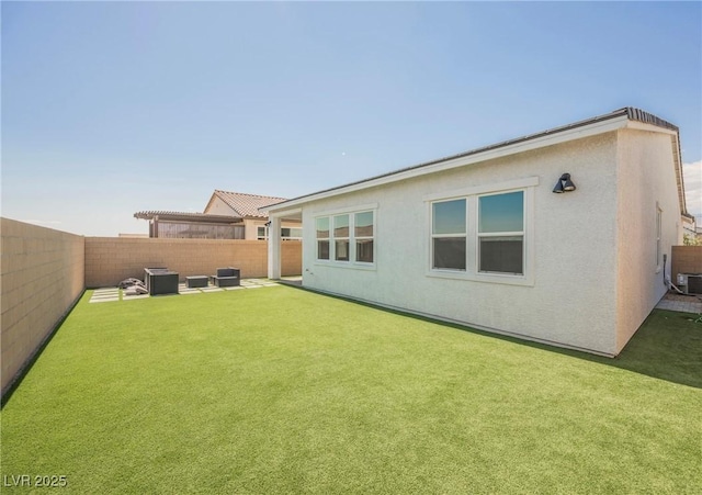 back of property featuring a fenced backyard, central AC unit, stucco siding, and a yard