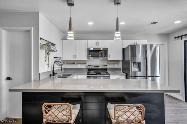 kitchen with white cabinets, appliances with stainless steel finishes, light stone counters, a sink, and a peninsula