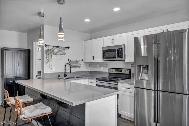 kitchen with light stone counters, a sink, stainless steel appliances, white cabinetry, and a peninsula