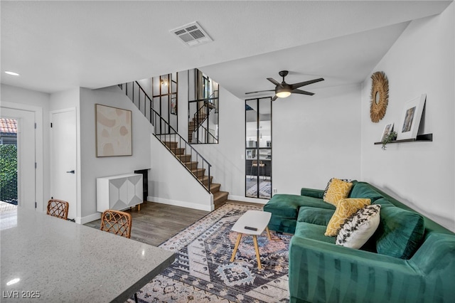 living room with visible vents, wood finished floors, baseboards, stairway, and a ceiling fan
