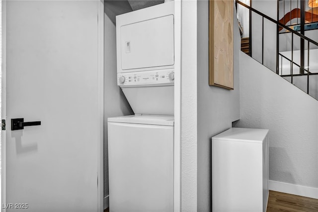clothes washing area with baseboards, laundry area, wood finished floors, and stacked washer / dryer