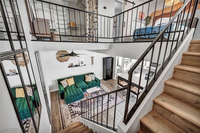 stairway featuring a high ceiling, ceiling fan, and wood finished floors