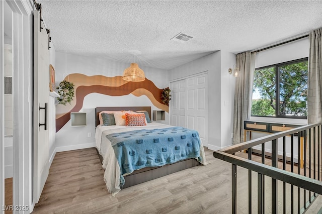bedroom with a textured ceiling, a closet, wood finished floors, and visible vents