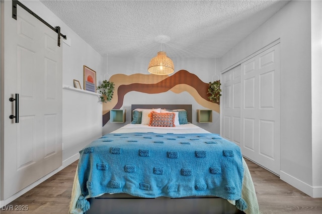 bedroom featuring a closet, a barn door, a textured ceiling, and wood finished floors