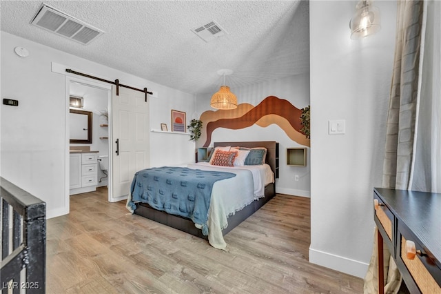 bedroom with a textured ceiling, visible vents, a barn door, and wood finished floors