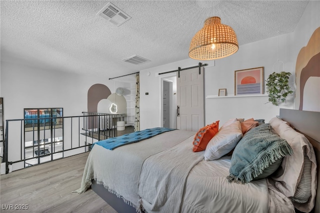 bedroom featuring a textured ceiling, visible vents, a barn door, and wood finished floors
