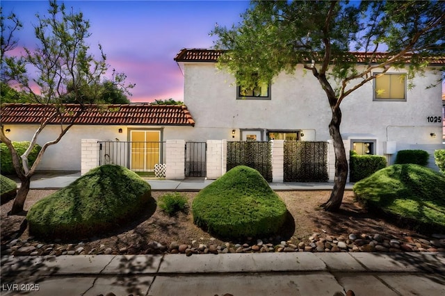 mediterranean / spanish house with stucco siding, a tiled roof, and fence