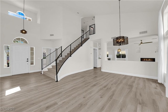 foyer entrance featuring visible vents, stairs, a towering ceiling, light wood-style floors, and a ceiling fan