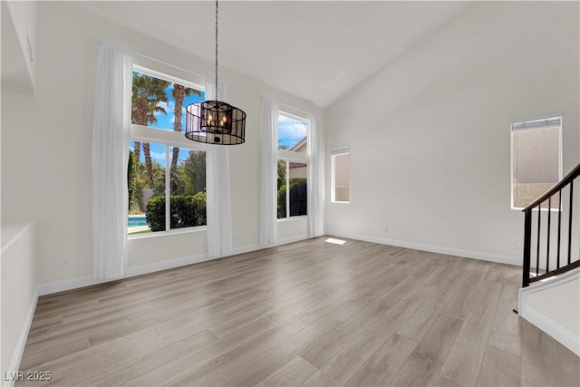 unfurnished dining area featuring light wood-type flooring, stairway, high vaulted ceiling, baseboards, and a chandelier