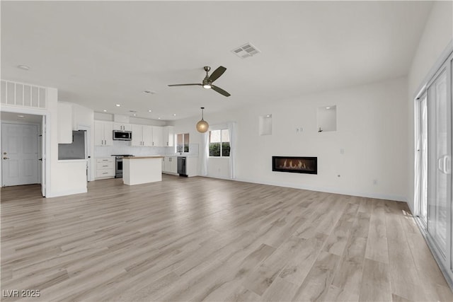 unfurnished living room with ceiling fan, visible vents, light wood-type flooring, a glass covered fireplace, and recessed lighting
