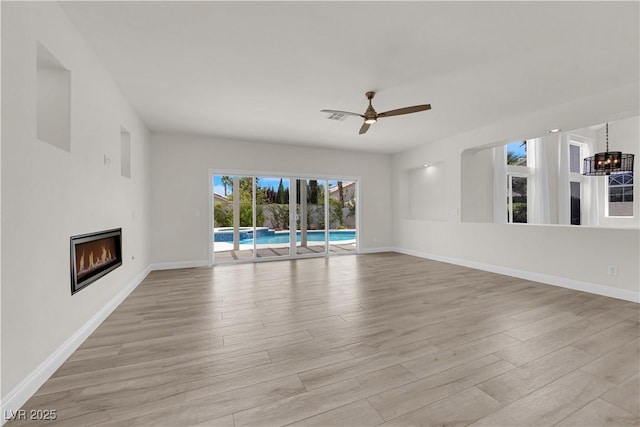 unfurnished living room with baseboards, a glass covered fireplace, and light wood-style flooring