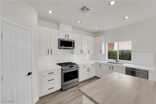 kitchen with visible vents, appliances with stainless steel finishes, tasteful backsplash, a sink, and white cabinetry