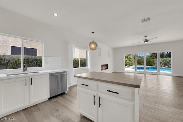 kitchen featuring a glass covered fireplace, wooden counters, open floor plan, stainless steel dishwasher, and visible vents