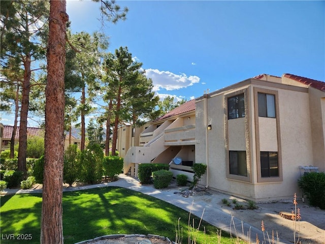 view of side of home featuring stairs, stucco siding, a yard, and a tiled roof