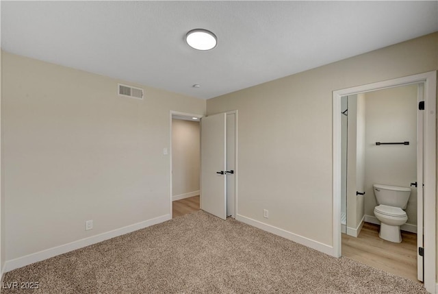 unfurnished bedroom featuring light colored carpet, baseboards, and ensuite bath