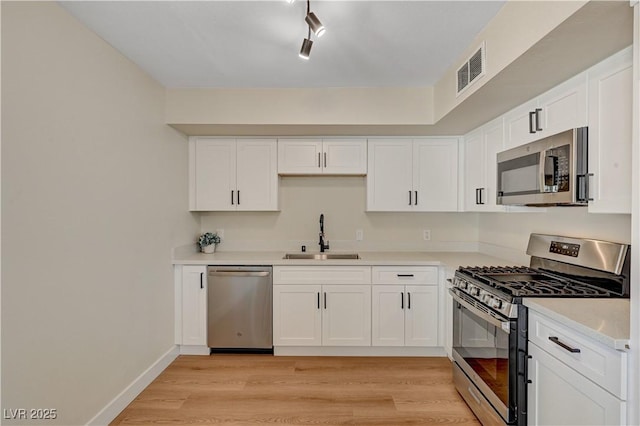 kitchen featuring a sink, appliances with stainless steel finishes, light wood-style flooring, white cabinetry, and light countertops