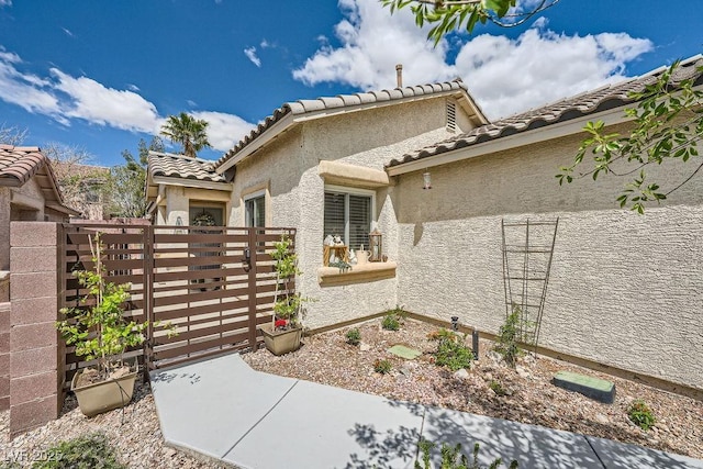 view of side of home with fence private yard, a gate, stucco siding, and a tiled roof