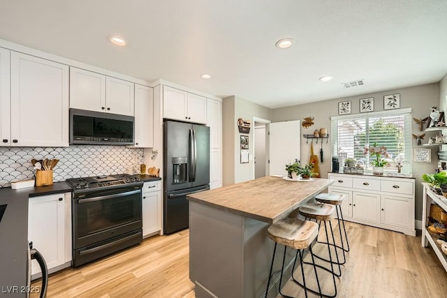 kitchen featuring white cabinets, light wood-style floors, tasteful backsplash, visible vents, and black appliances