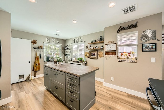 kitchen featuring visible vents, light wood-style flooring, baseboards, a kitchen island, and gray cabinetry