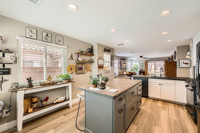 kitchen with white cabinets, a sink, light wood-style floors, dishwasher, and a center island