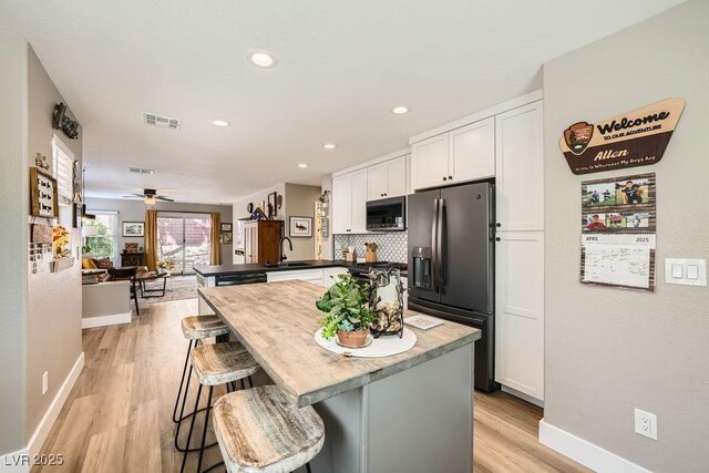 kitchen featuring visible vents, a sink, stainless steel microwave, black fridge, and white cabinetry