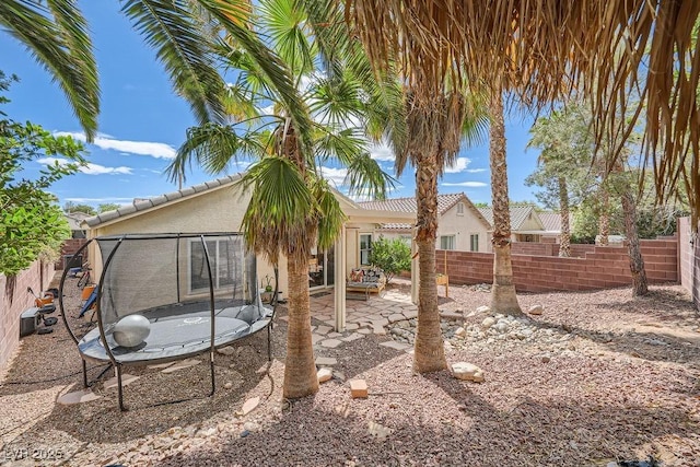 rear view of house featuring a trampoline, stucco siding, a fenced backyard, a patio area, and a tiled roof